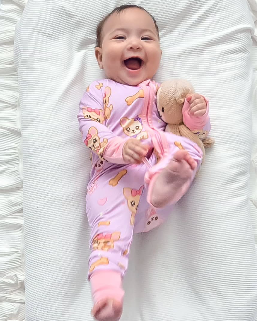 Happy baby wearing our Chiwidreams Bamboo Zip Romper lying on a soft white ruffle cushion holding a teddy bear