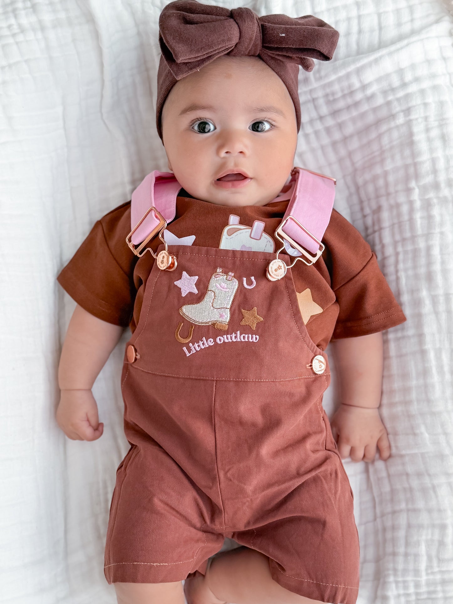 Little Violet Threads Little Outlaw baby overalls in rust pink with embroidered western design on baby model