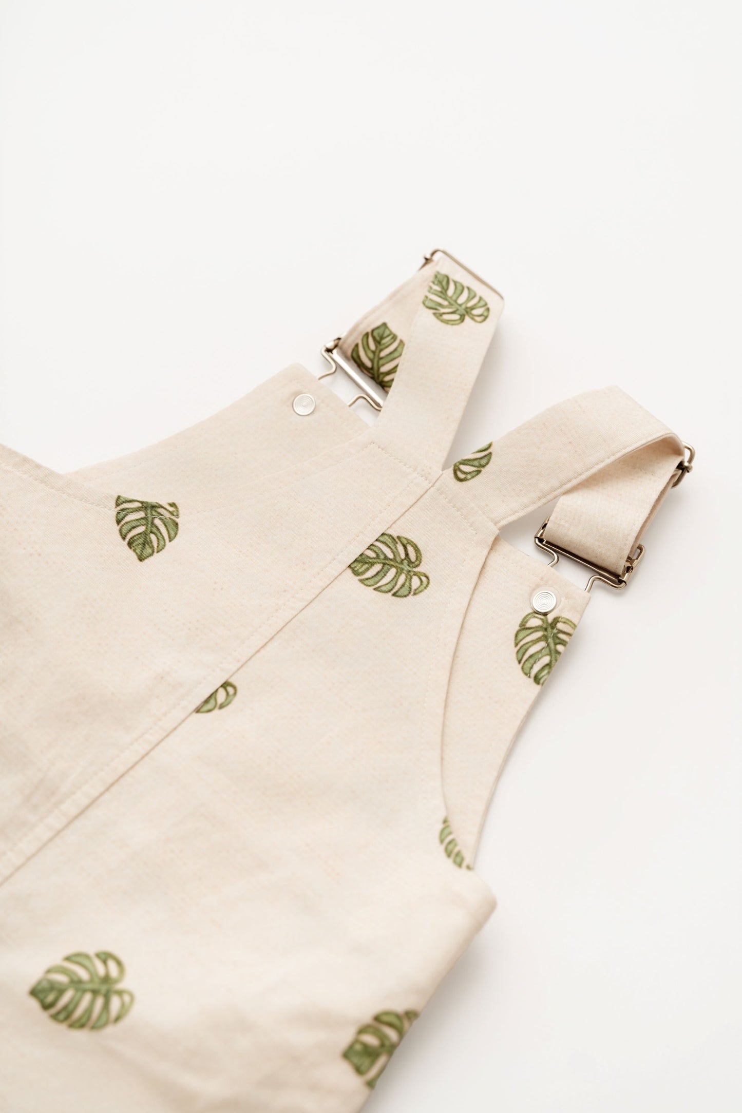 Beige Monstera Baby Overalls cotton leaf infant overalls angled flat lay on white background