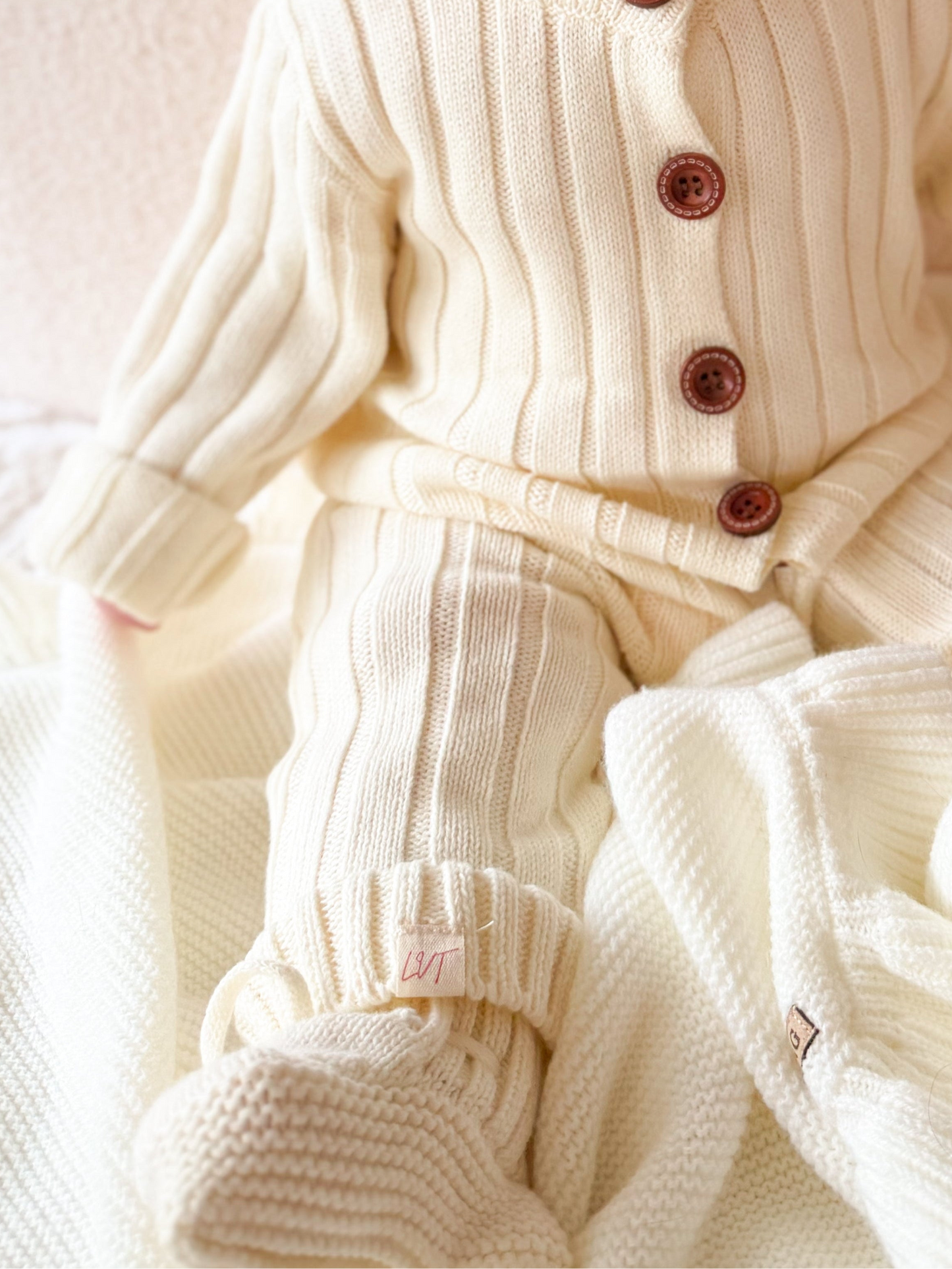 Close up of Vanilla Marshmallow baby knit booties in soft cream cotton knit with matching outfit and blanket