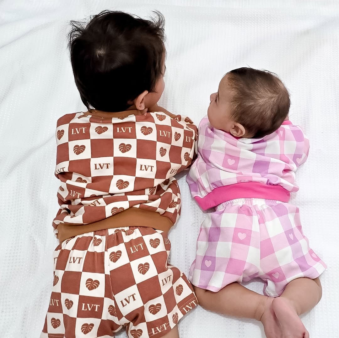 Two children wearing matching checkered outfits on a white blanket.