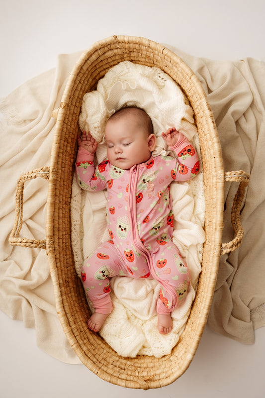 Sleeping baby in woven bassinet wearing pink Strawberry Matcha bamboo zip romper
