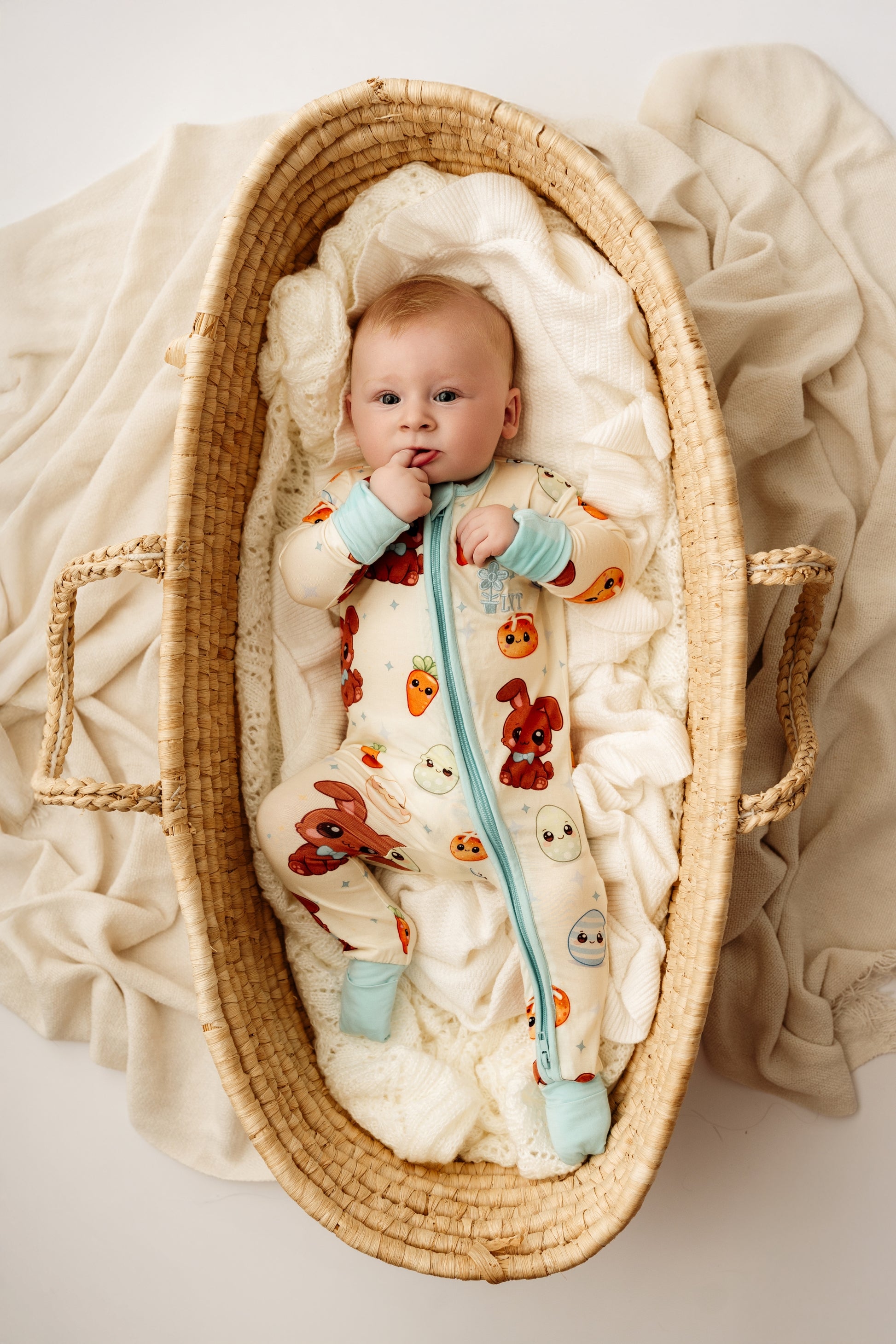 Baby wearing Blue Bunny bamboo zip romper lying in woven bassinet