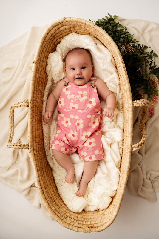 Baby wearing Violet Overalls pink floral baby outfit lying in woven bassinet