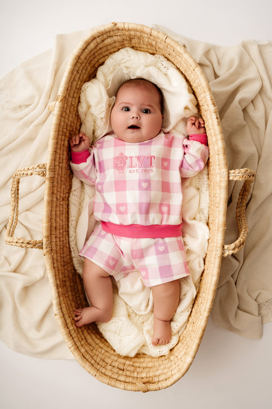 Baby wearing pink check two piece lounge set lying in woven bassinet