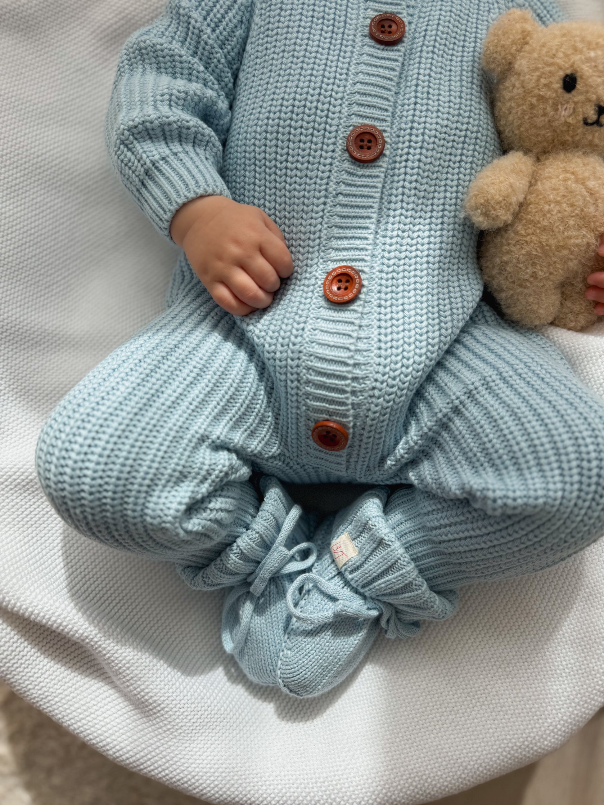Blue Haven cotton knit baby booties styled with matching blue knit outfit and teddy bear