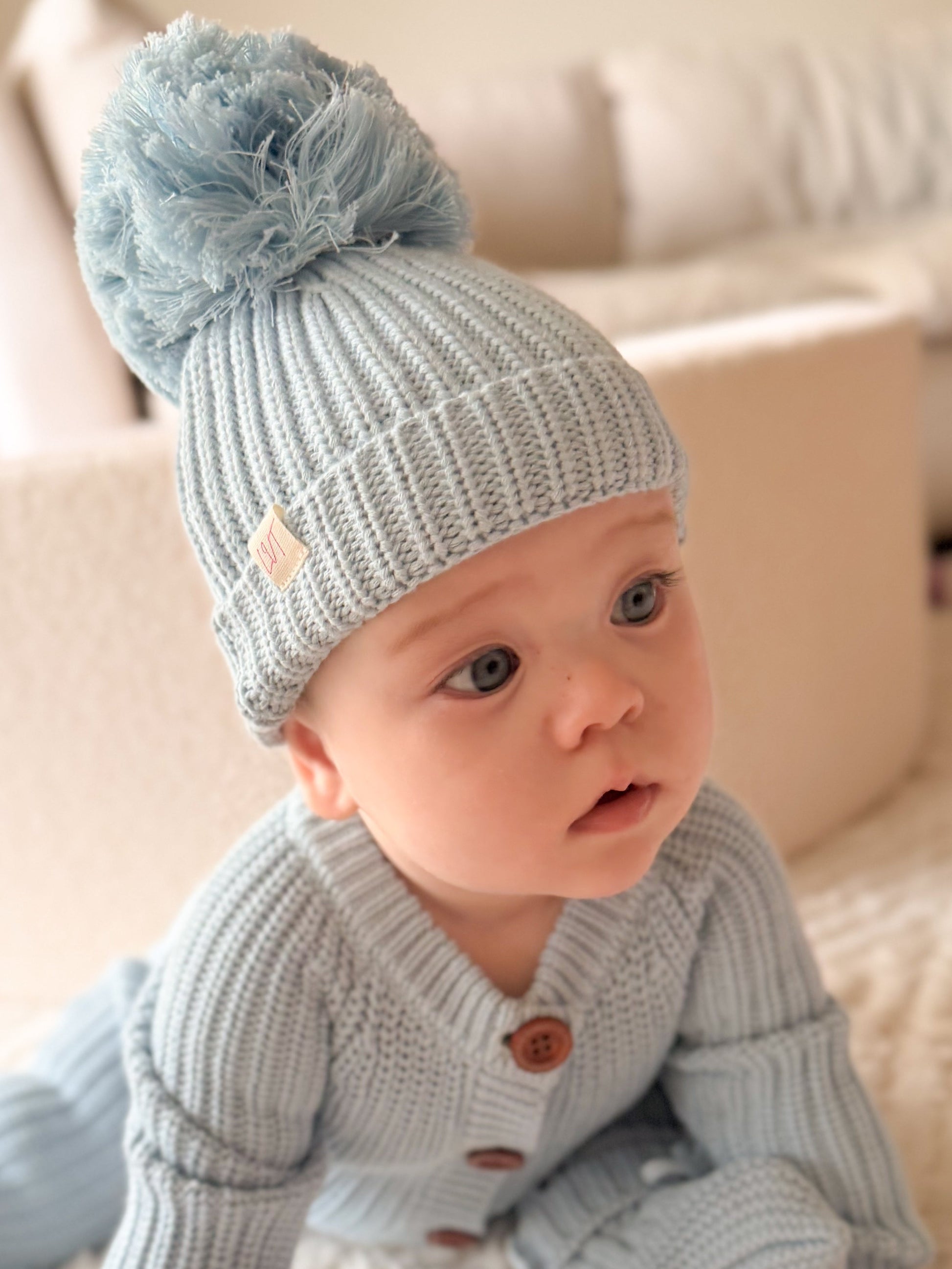Blue Haven knit baby beanie with fluffy pom pom styled on baby wearing matching blue cotton knit outfit