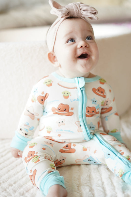 Baby wearing our blue cowboy outlaw bamboo zippy romper with exclusive western print, sitting on a soft cream blanket