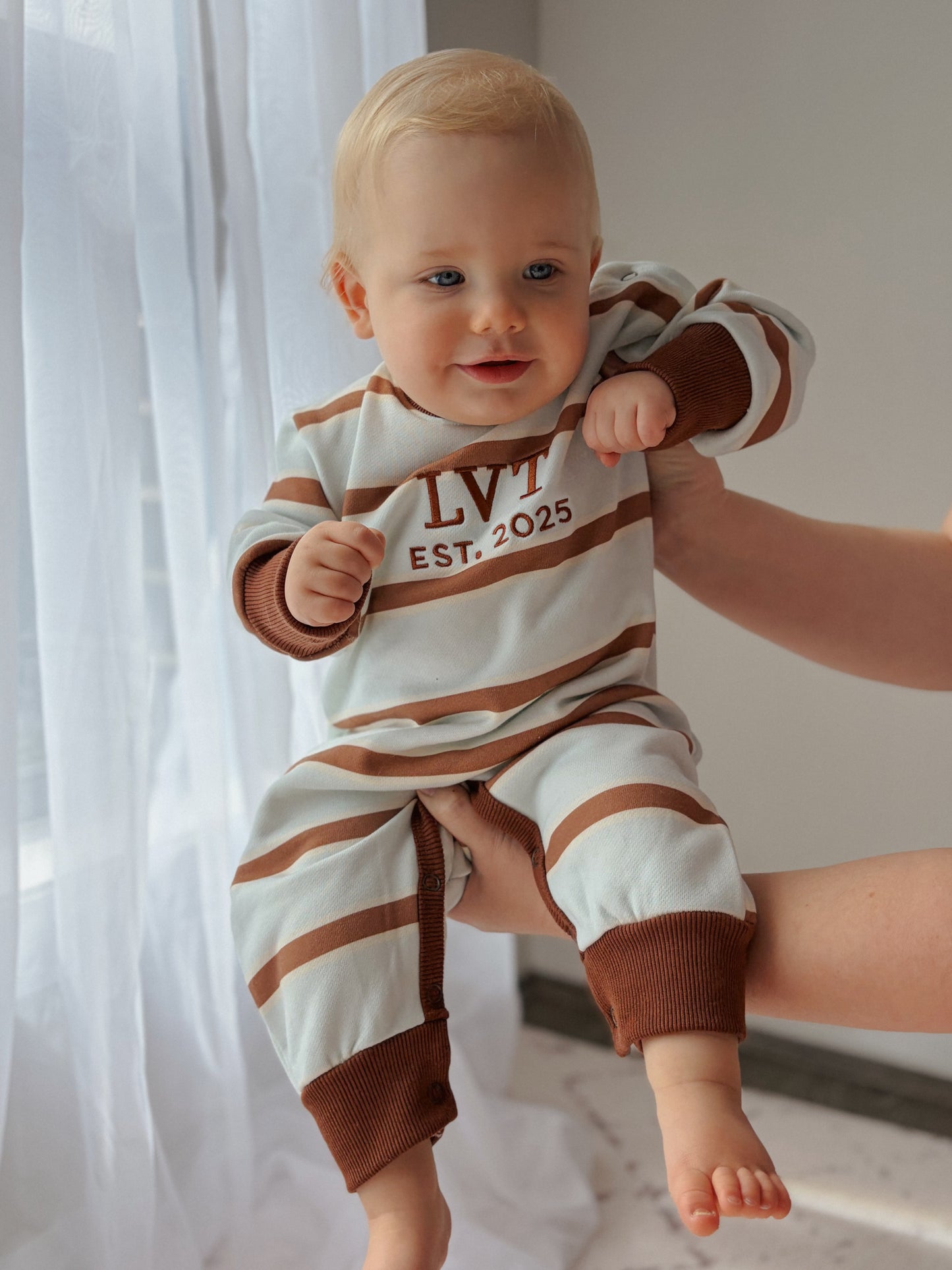 Bubblegum French Terry baby romper by Little Violet Threads featuring an oversized fit, embroidered logo and blue, cream and chocolate stripes.