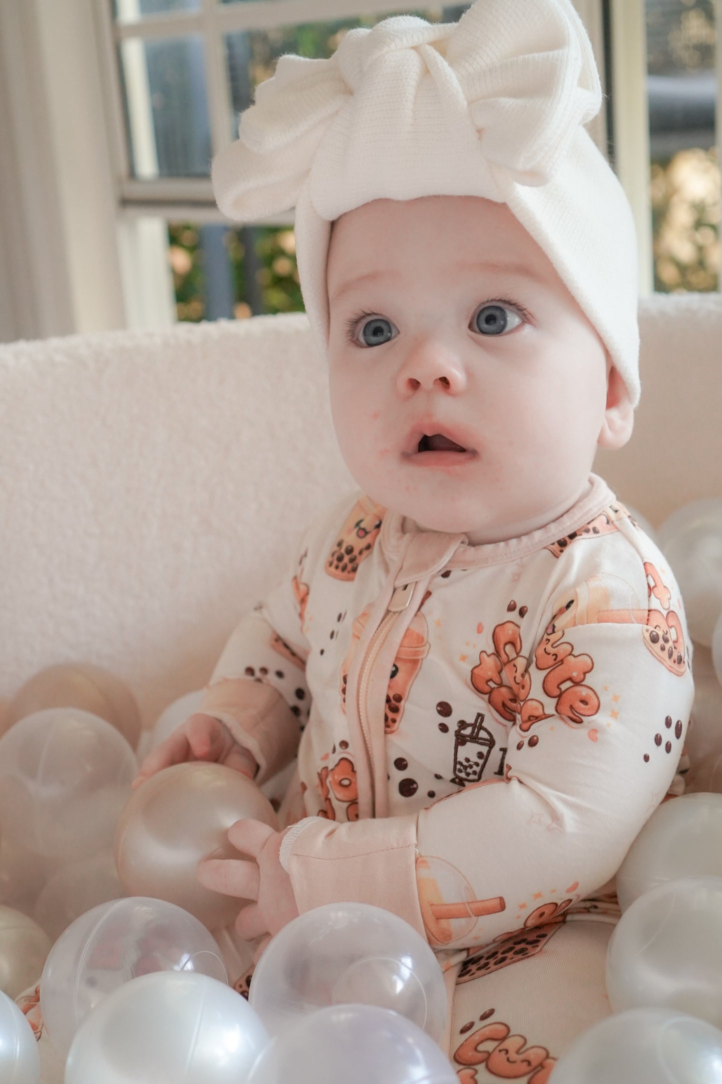 baby wearing little violet threads bubble tea baby bamboo zippy romper sitting with white balloons