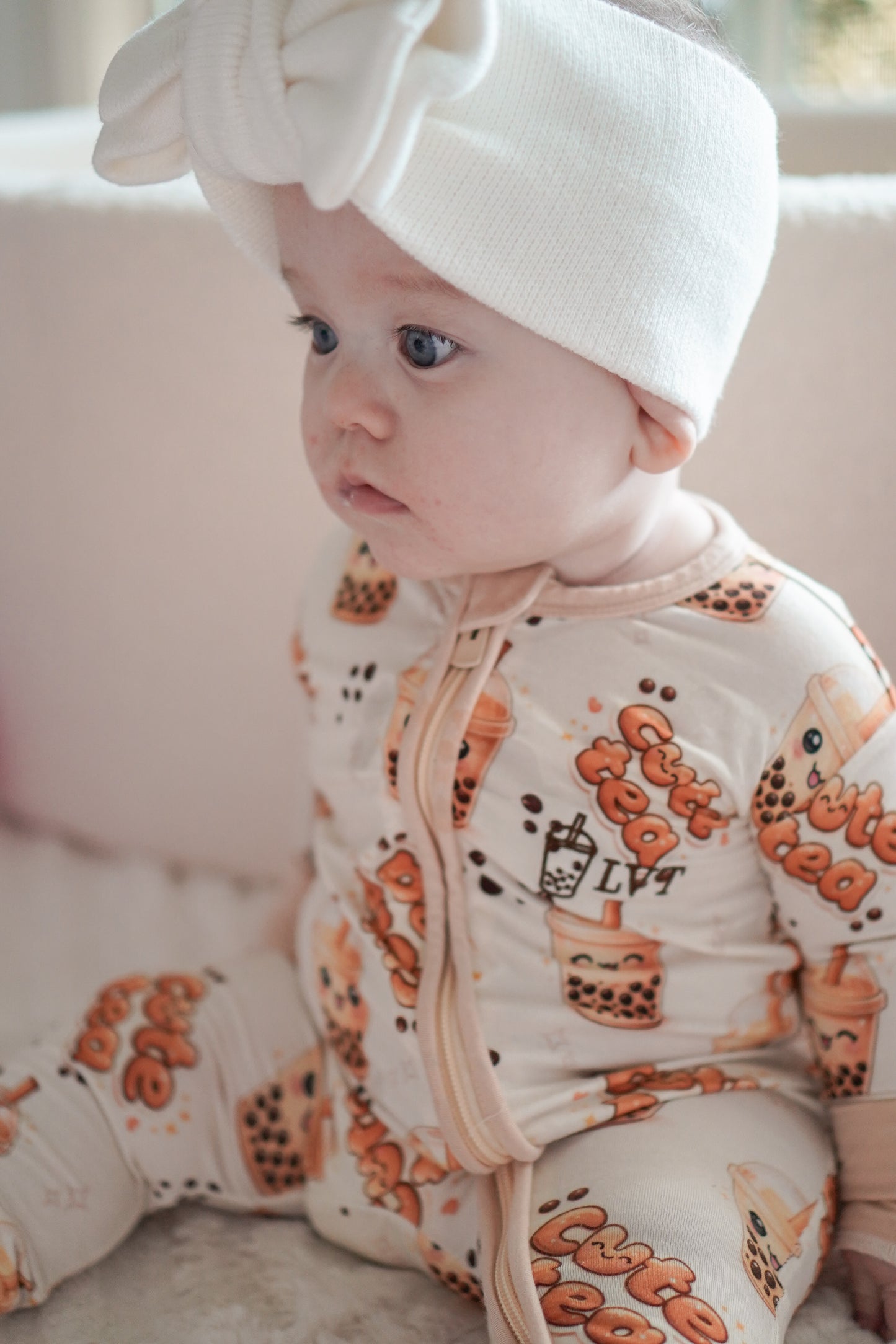 baby wearing little violet threads bubble tea baby bamboo zippy romper sitting in side profile with white bow headwrap