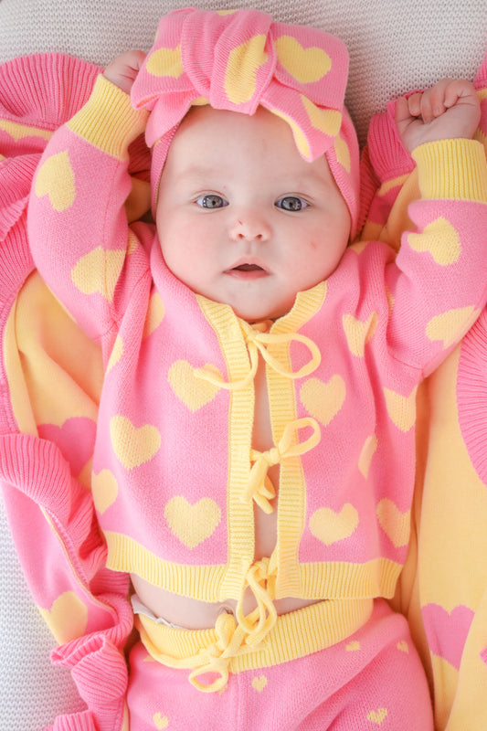 Close-up of baby wearing the Buttercup Princess pink and yellow cotton knit set with matching oversized headbow