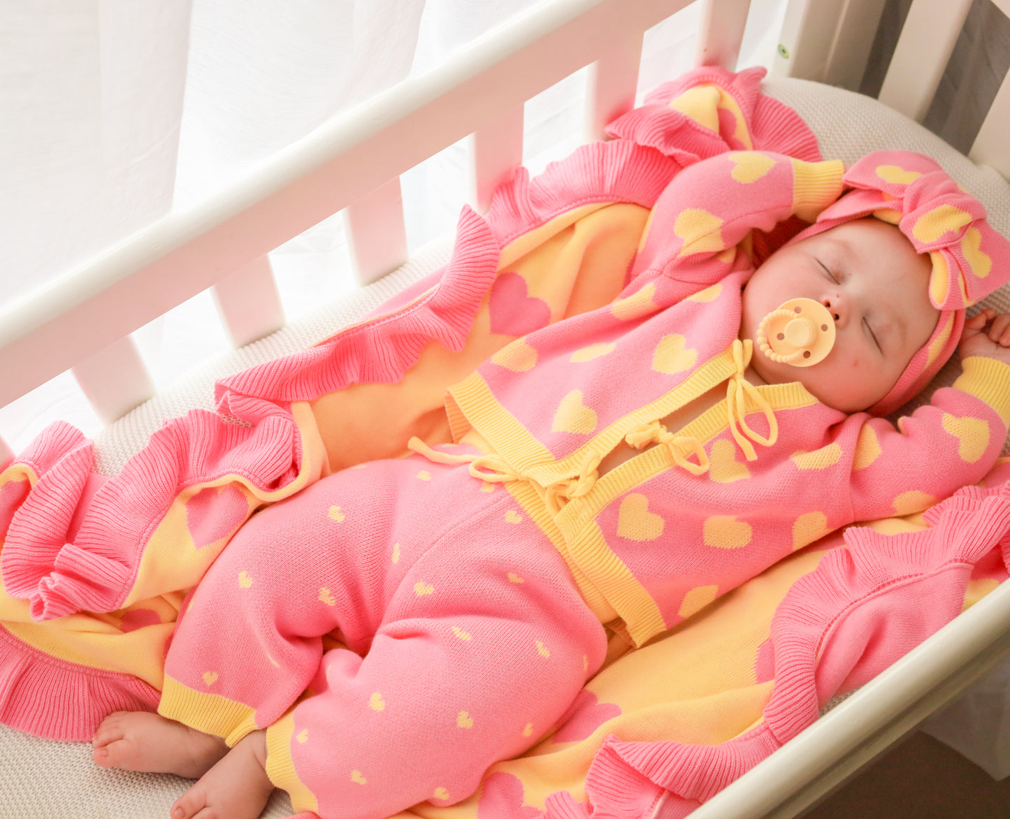 Baby girl wearing the Buttercup Princess pink and yellow cotton knit set with matching headbow and blanket