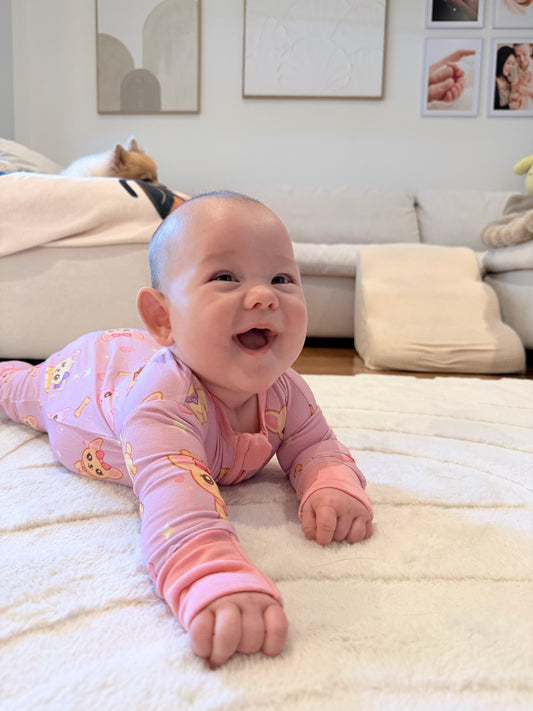 Smiling baby wearing our Chiwidreams Bamboo Zip Romper lying on a soft cream play mat in a cosy home setting