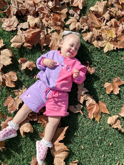 Toddler girl lying on autumn leaves wearing the Little Violet Threads La Dolce Lollie colourblock sweat set in pink and lilac