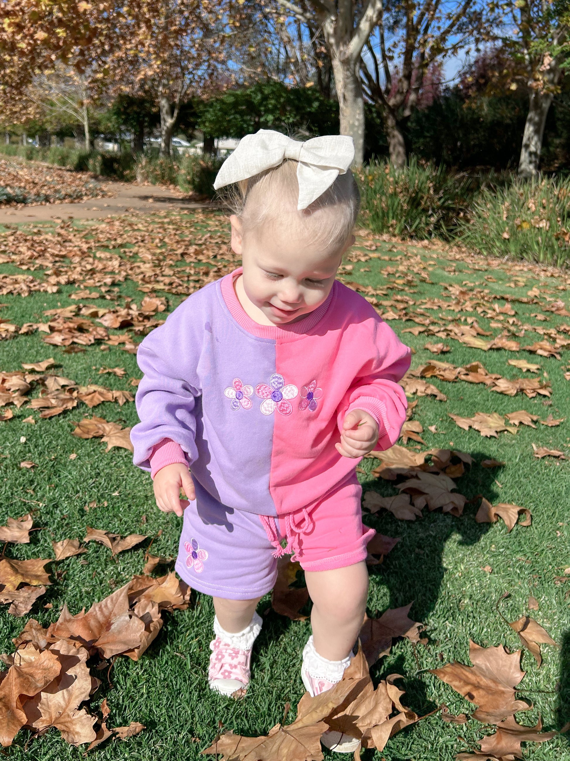 Toddler girl wearing the Little Violet Threads La Dolce Lollie colourblock sweat set standing outdoors among autumn leaves