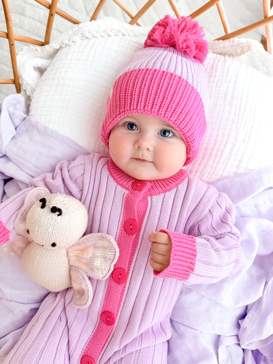 Baby girl in La Dolce Lollie Dream cotton knit romper and pink pom pom beanie