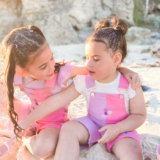 Girls wearing La Dolce Lollie pink floral overalls by Little Violet Threads at the beach.