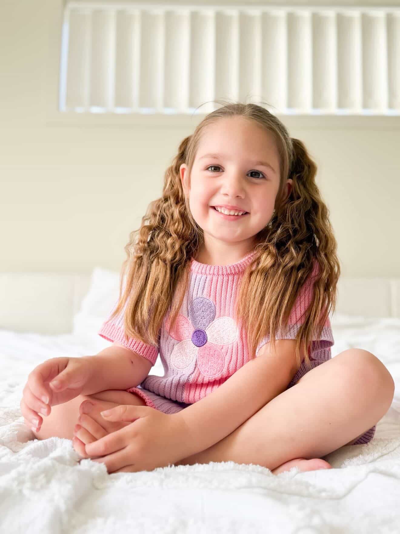 Young girl sitting on a bed wearing the Little Violet Threads La Dolce Lollie Petal Knit Set in pink and lilac