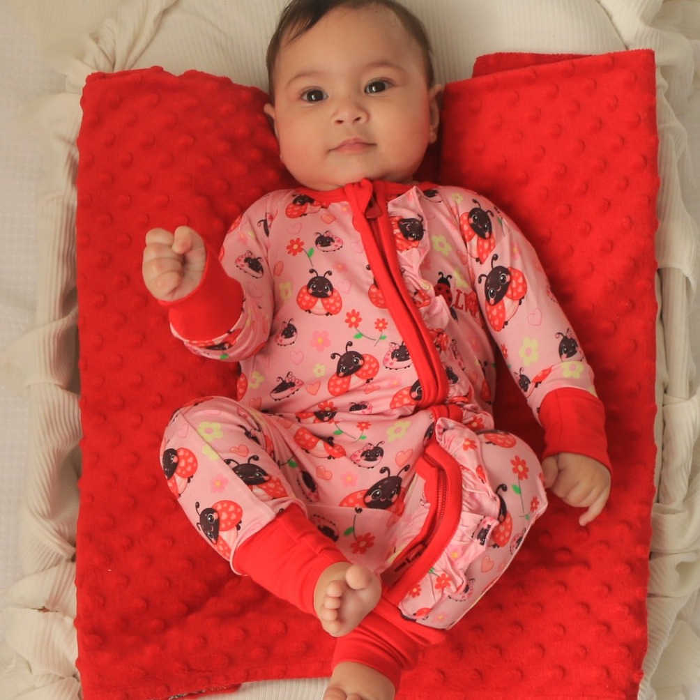 baby wearing little violet threads lady bug baby bamboo zippy romper lying on red blanket