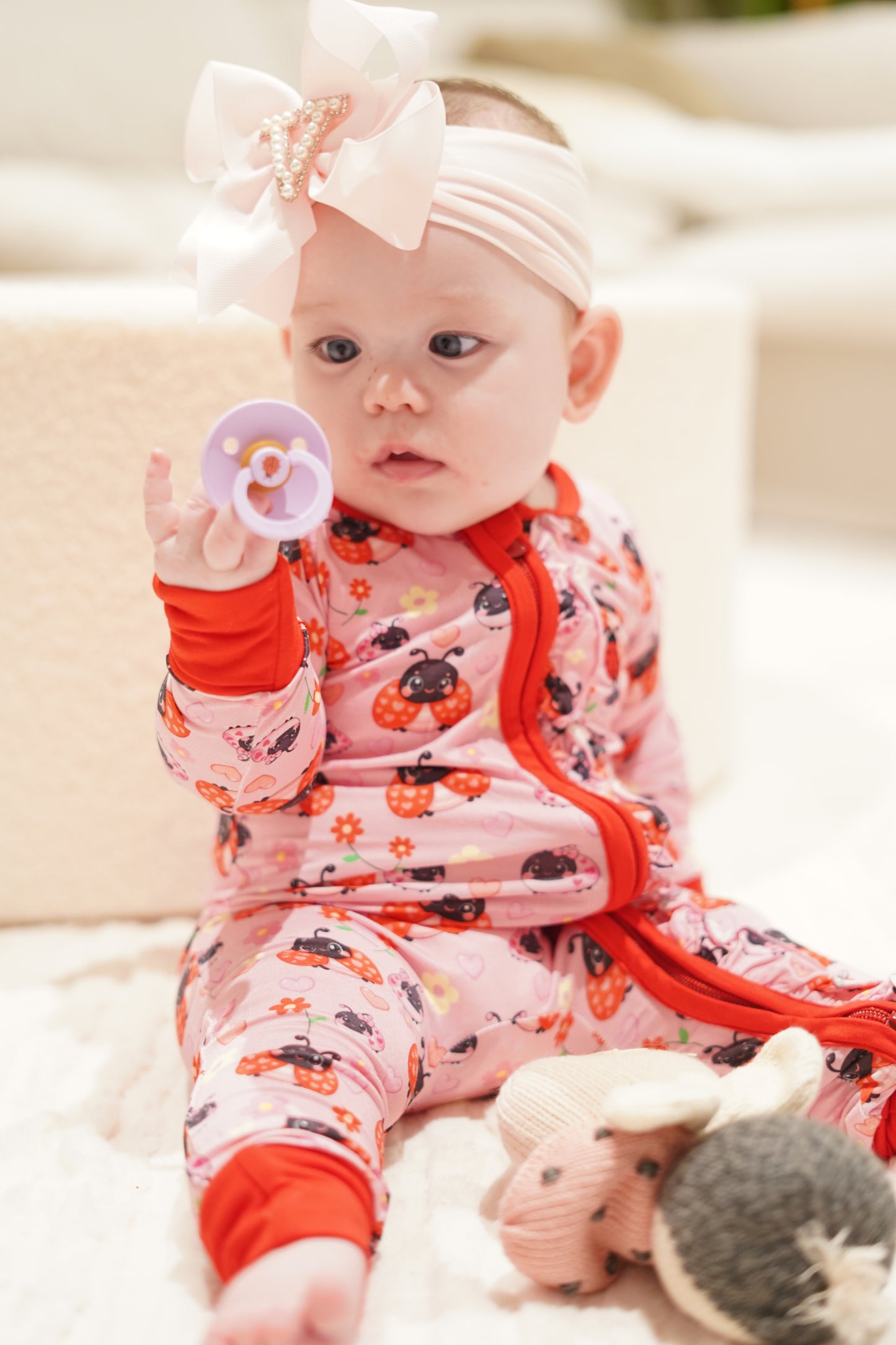 baby wearing little violet threads lady bug baby bamboo zippy romper sitting with toy