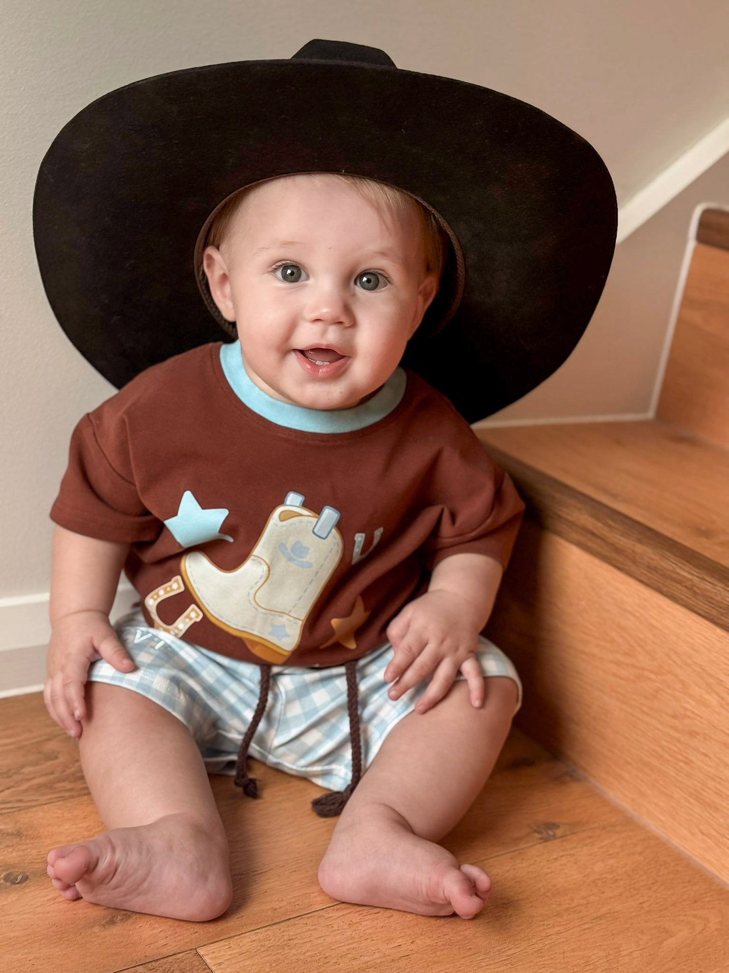 Baby wearing Little Violet Threads Little Outlaw boys two piece set with blue gingham shorts and western graphic tee