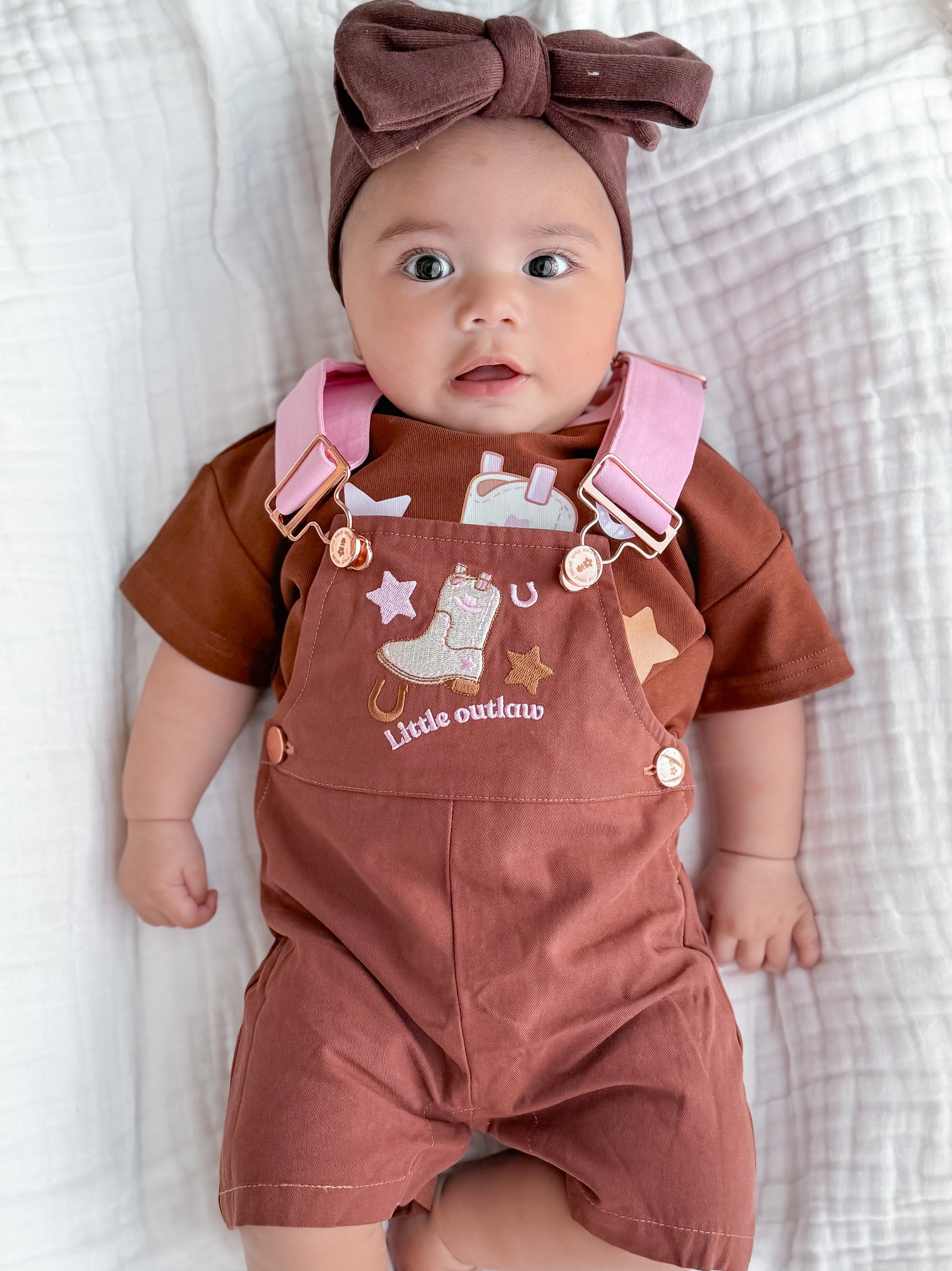 Little Violet Threads Little Outlaw baby overalls in rust pink with embroidered western design on baby model