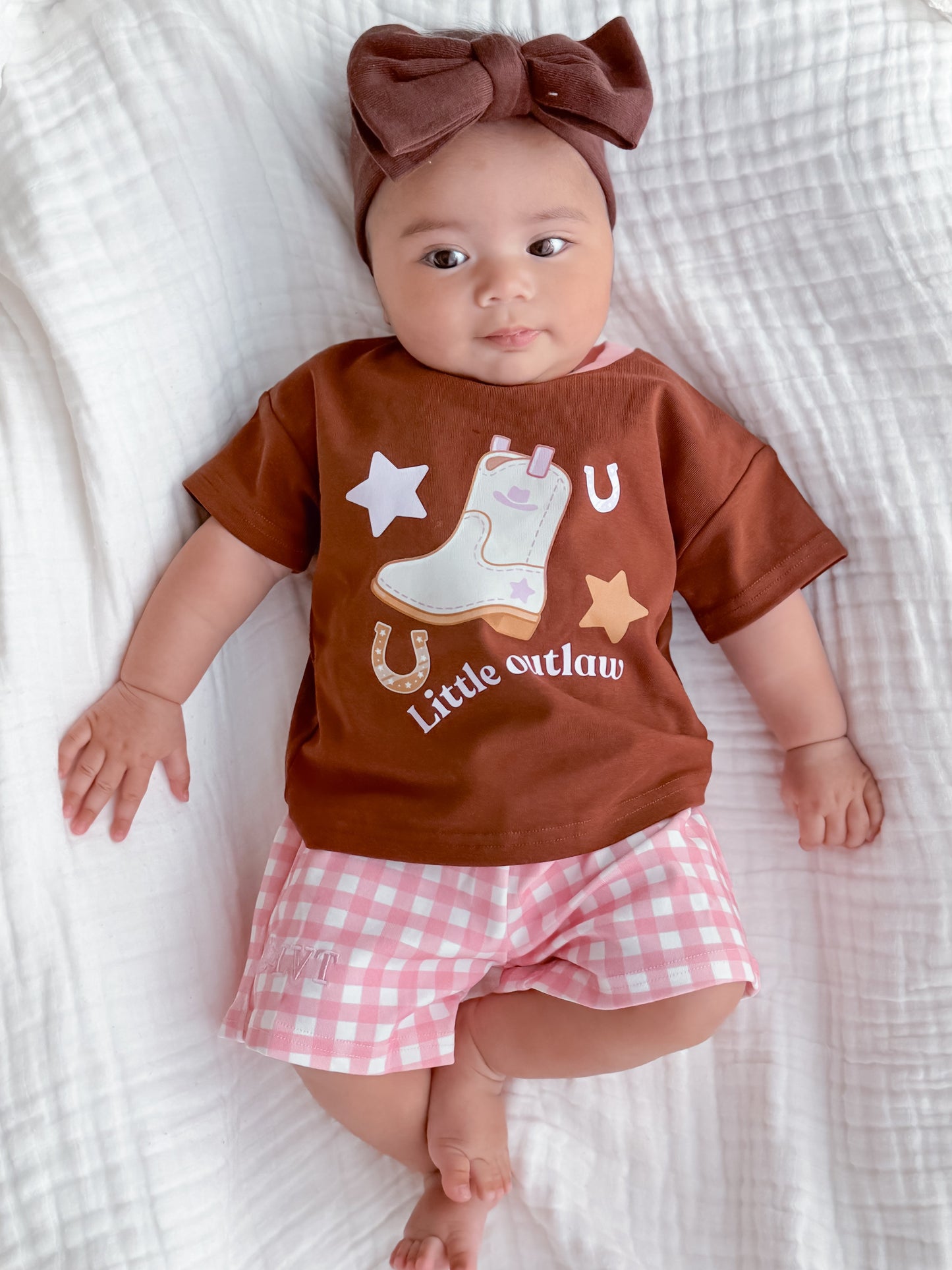 Baby wearing Little Violet Threads Little Outlaw two piece set with pink gingham shorts and western graphic tee