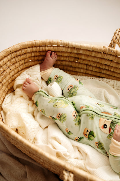 Baby in a moses basket wearing a green onesie with animal prints.