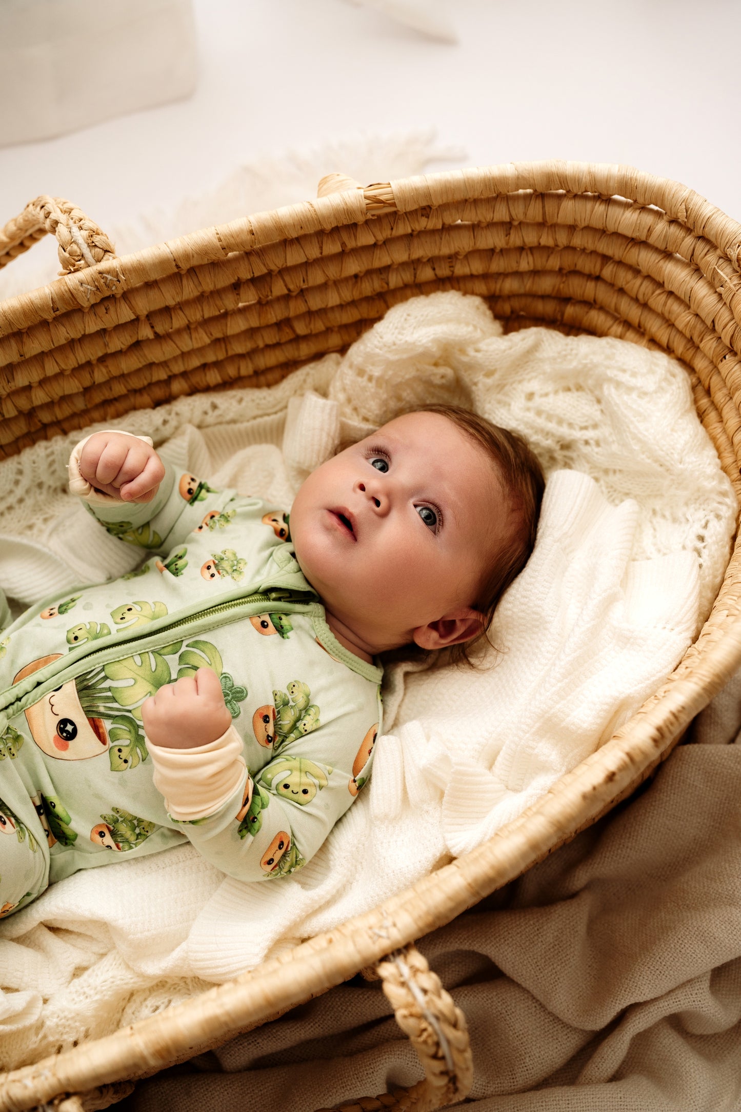 Baby in a crib wearing a green onesie with animal prints on a white blanket.
