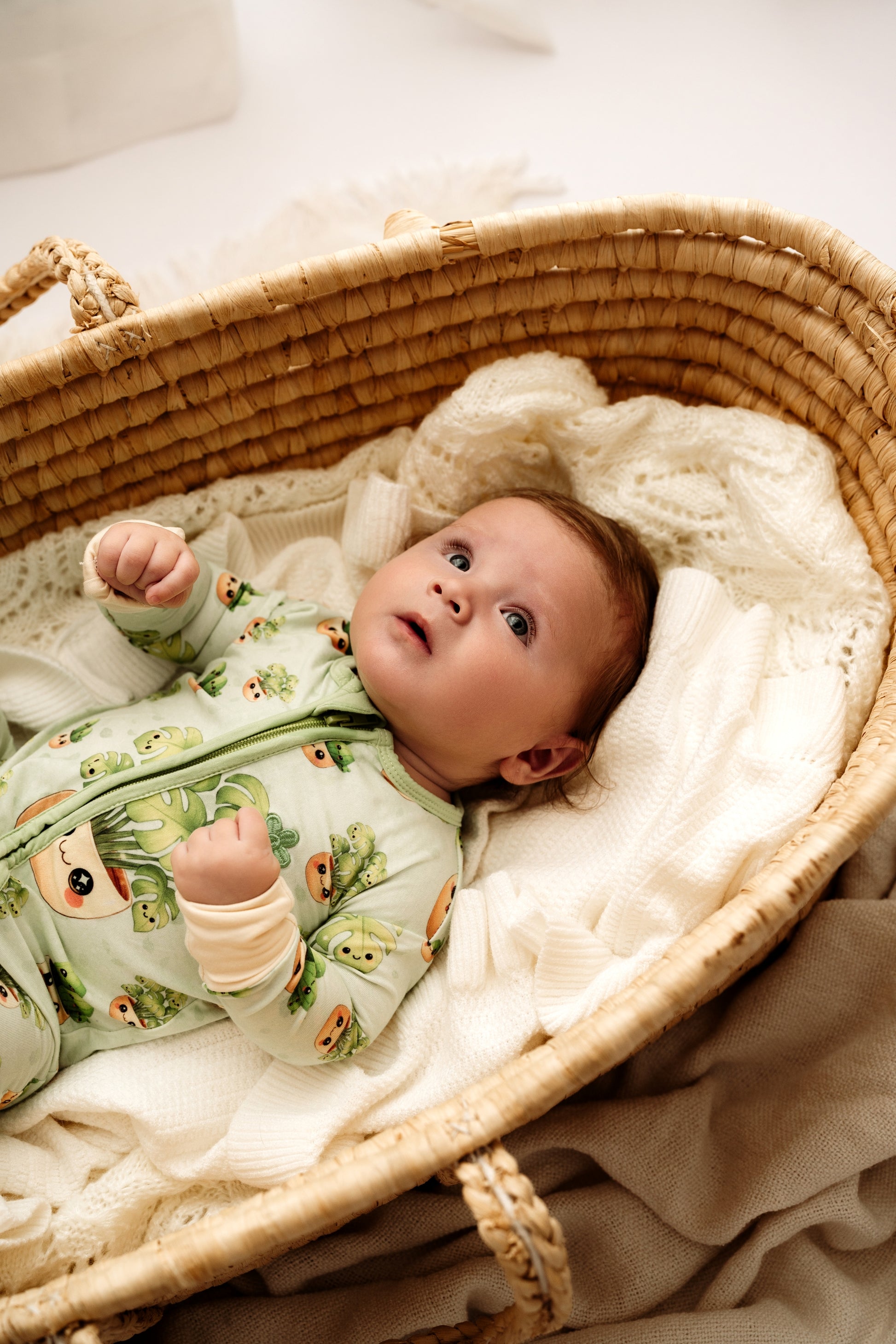 Baby in a crib wearing a green onesie with animal prints on a white blanket.