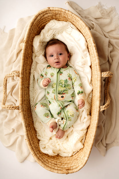 Baby in a green outfit lying in a wicker crib with white bedding