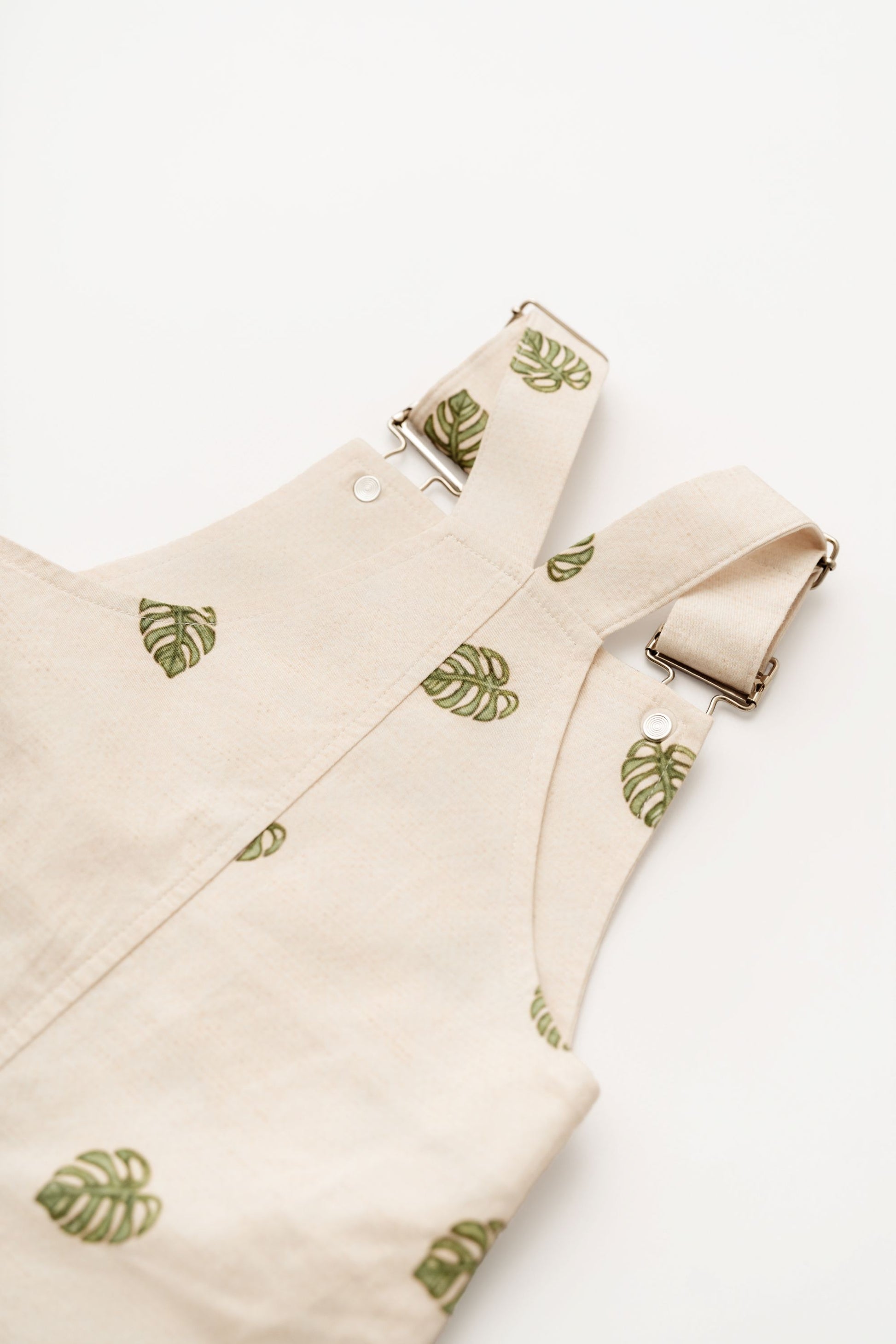Beige Monstera Baby Overalls cotton leaf infant overalls angled flat lay on white background