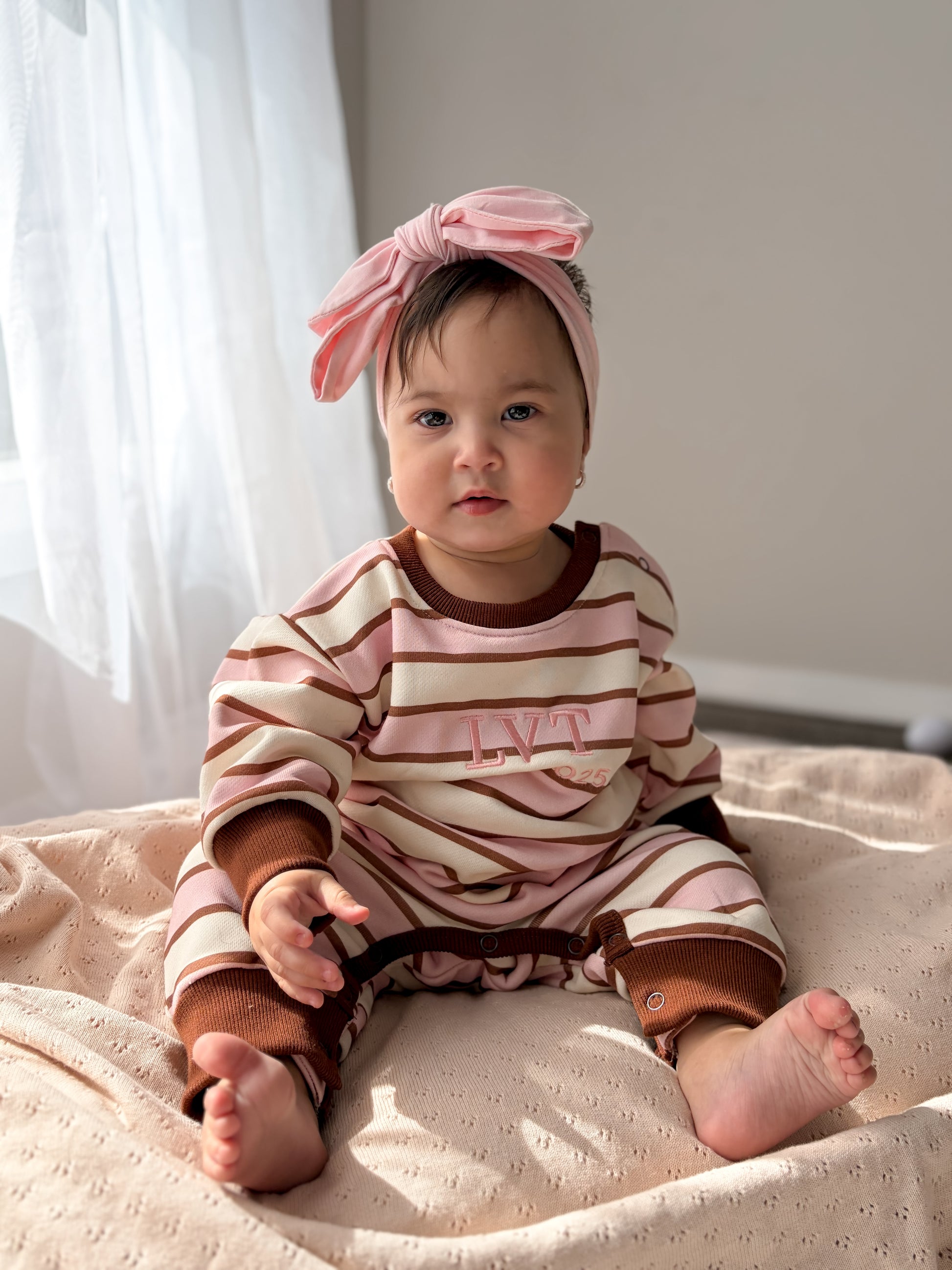 Baby wearing the Neapolitan French Terry romper by Little Violet Threads sitting on a soft blanket in pink, cream and chocolate stripes.