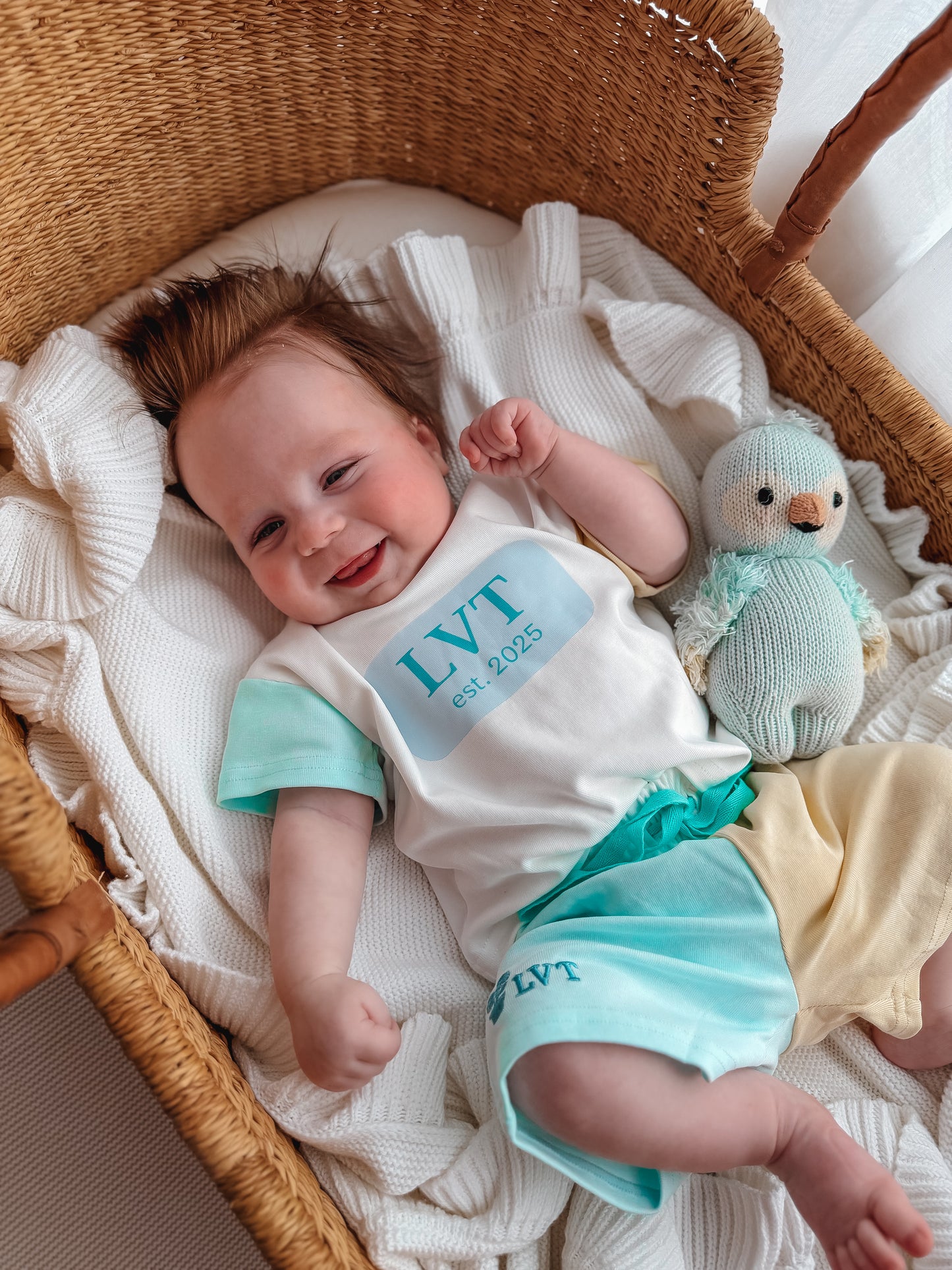 Baby wearing Little Violet Threads Pastel Maison lounge set with oversized tee and blue yellow colour block shorts in wicker bassinet