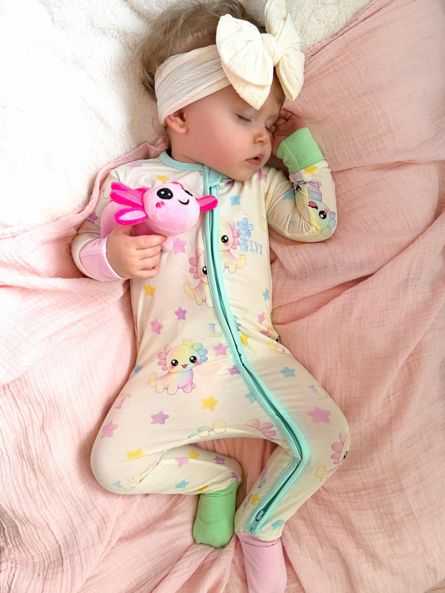 baby wearing little violet threads pastel bamboo baby zippy romper sleeping on pink blanket holding toy