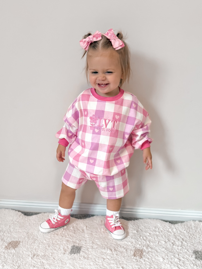Child wearing a pink checkered outfit with matching shoes on a neutral background