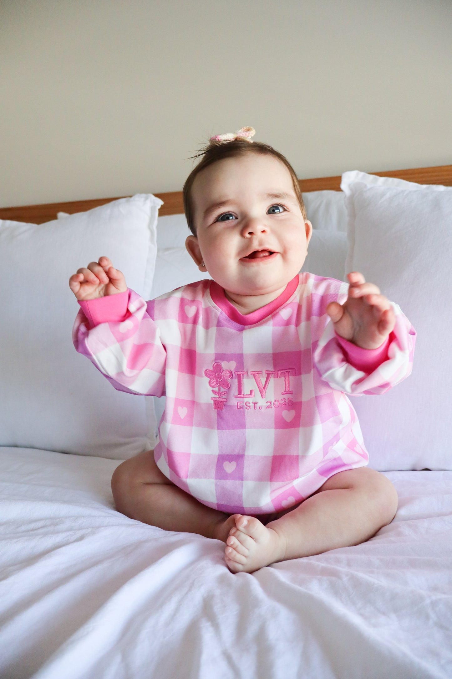Baby girl wearing Little Violet Threads Pink Sugar Lounge Set in pink gingham oversized jumper sitting on bed