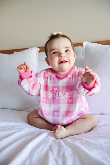 Baby girl wearing Little Violet Threads Pink Sugar Lounge Set in pink gingham oversized jumper sitting on bed