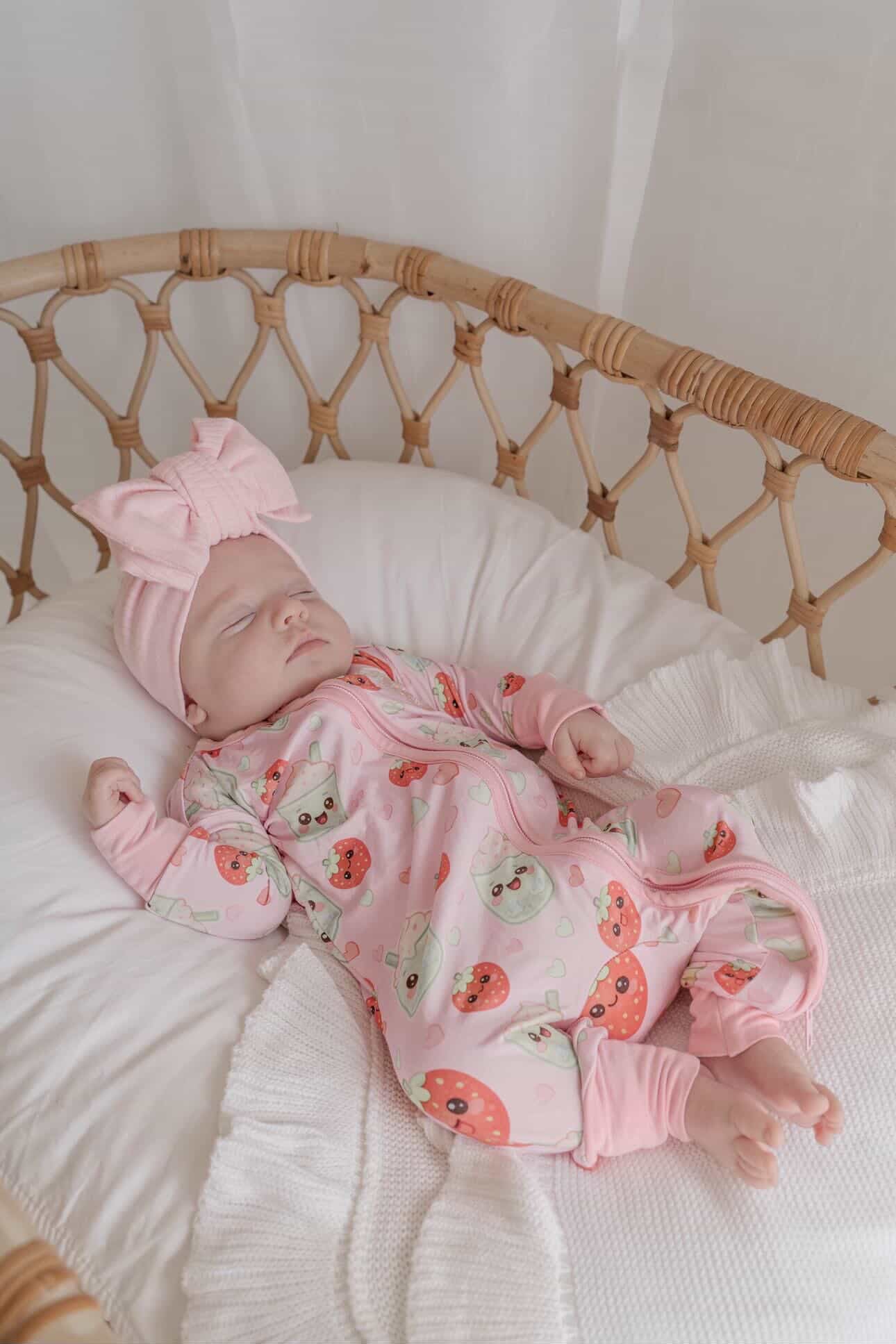 Baby wearing Strawberry Matcha bamboo zippy romper sleeping in wicker bassinet
