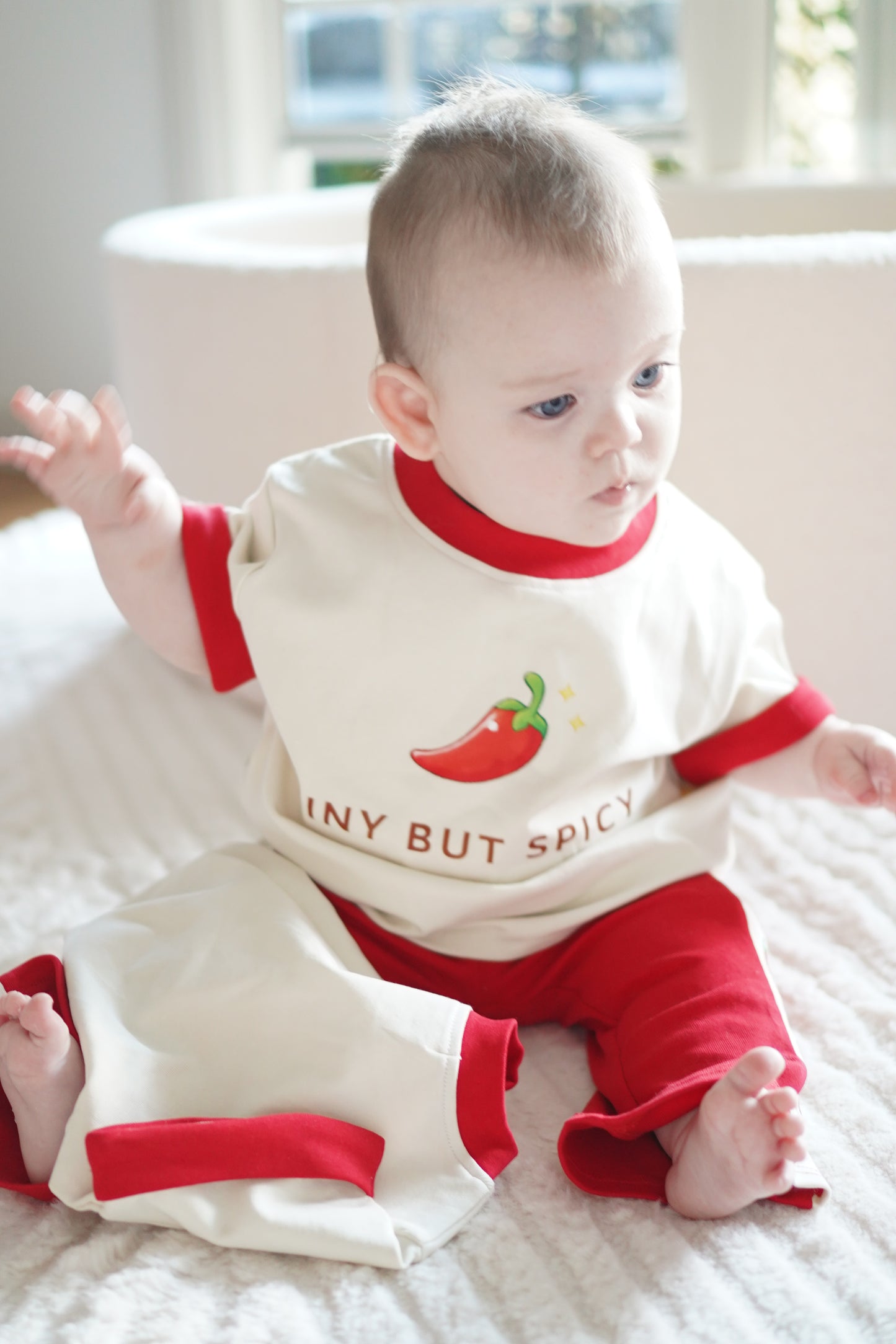 baby wearing little violet threads tiny but spicy tee and red flare pants set sitting on blanket