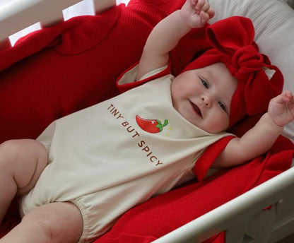 baby wearing little violet threads tiny but spicy romper with red bow headwrap