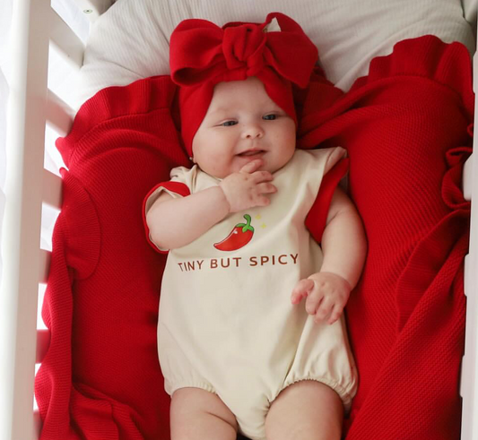 baby wearing little violet threads tiny but spicy oversized romper with red bow headband lying in cot