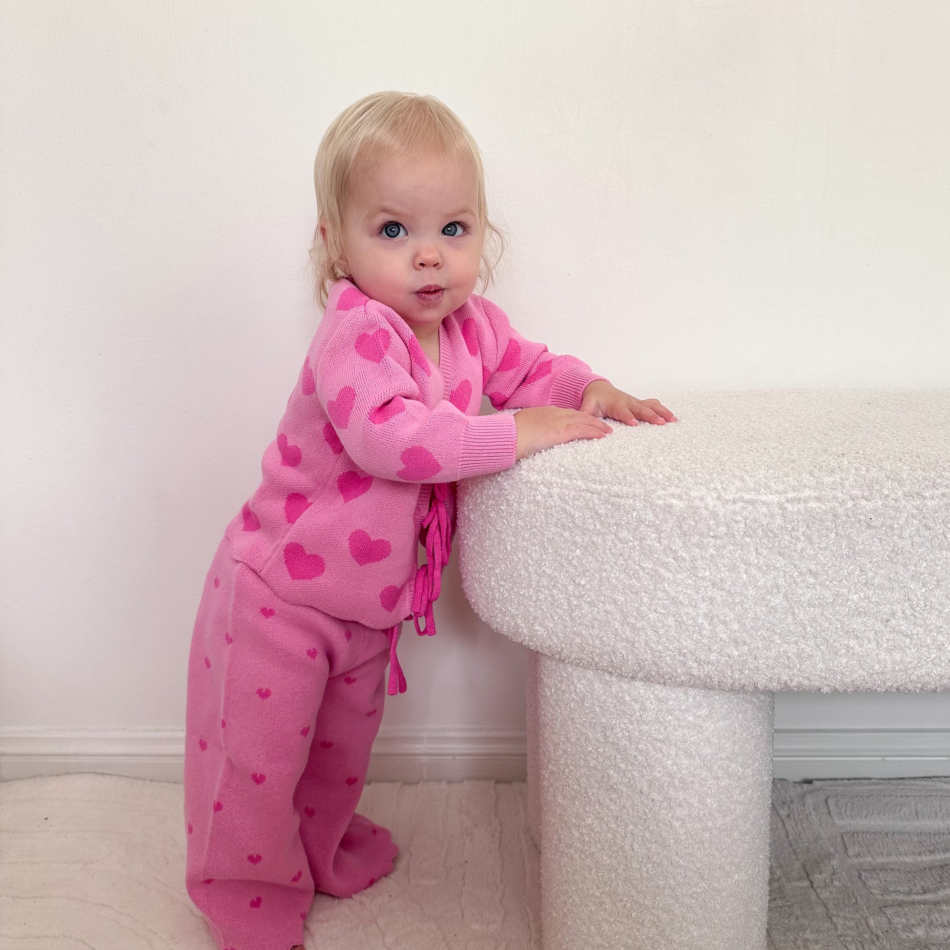 Toddler wearing the Little Violet Threads Valentina Knit Set in pink heart knit, standing beside textured white table