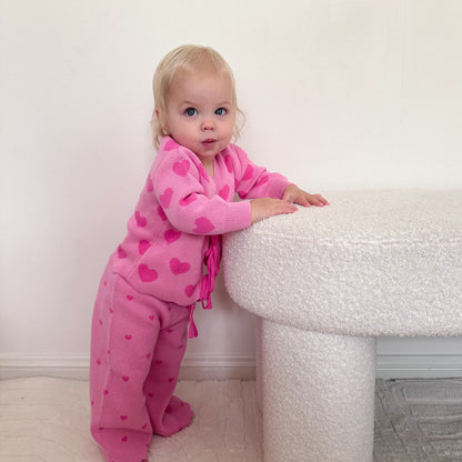 Toddler wearing the Little Violet Threads Valentina Knit Set in pink heart knit, standing beside textured white table