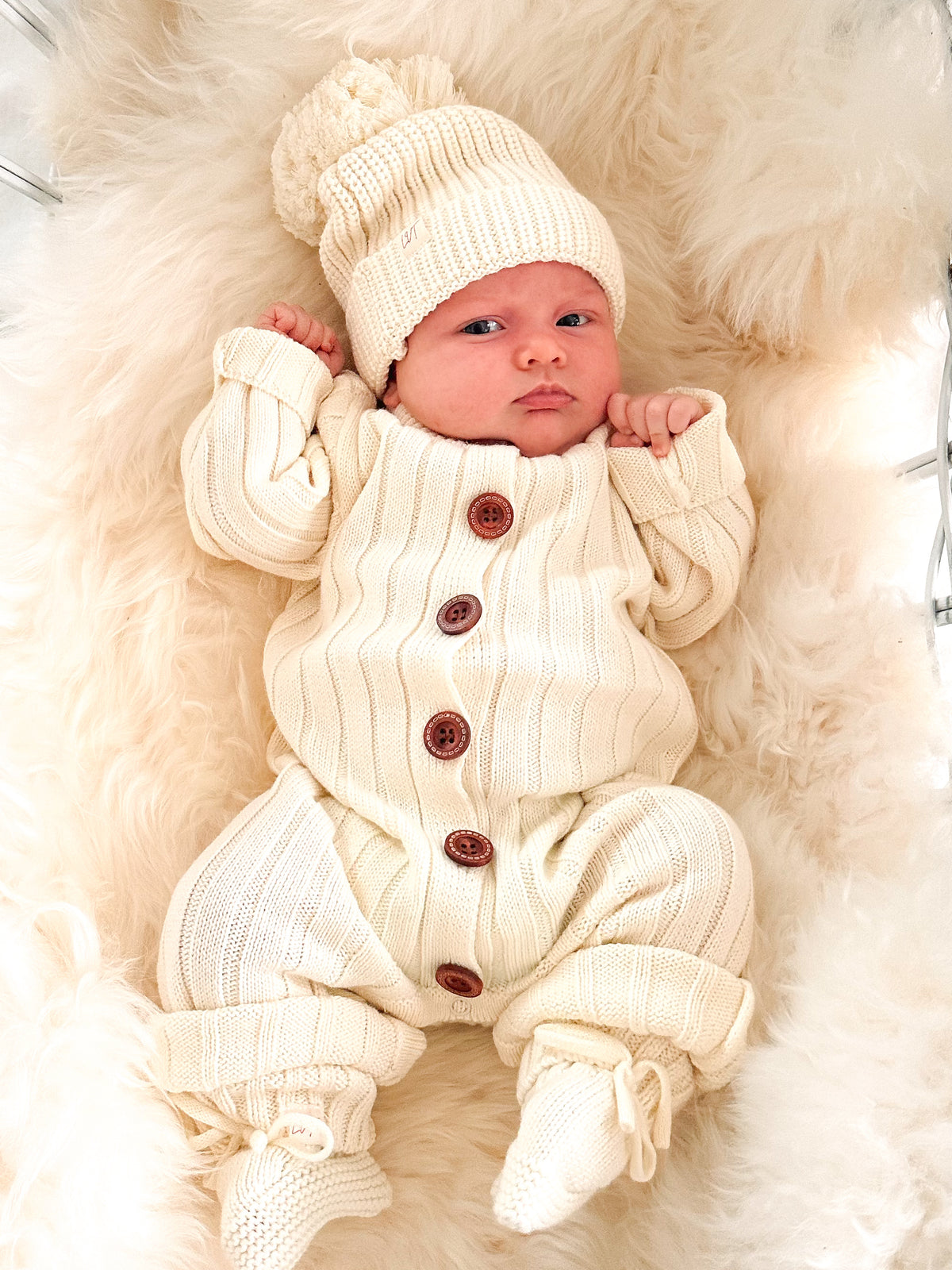 Newborn baby wearing the Vanilla Marshmallow cream ribbed cotton knit romper with wooden buttons, matching knit beanie and booties.