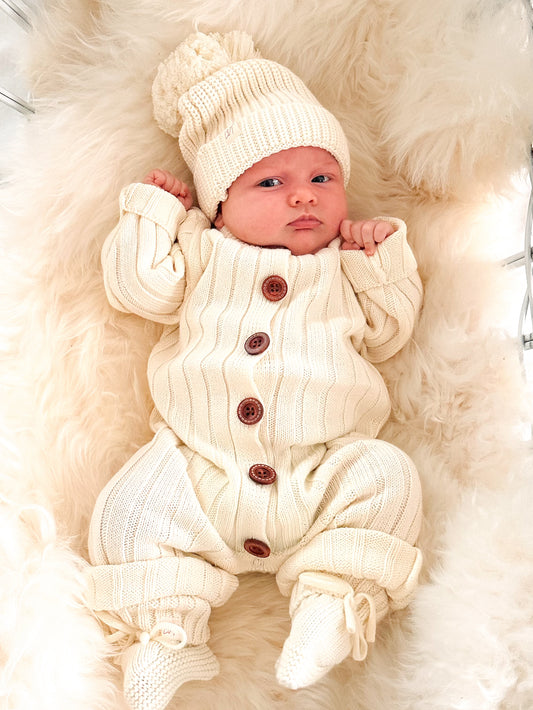Newborn baby wearing the Vanilla Marshmallow cream ribbed cotton knit romper with wooden buttons, matching knit beanie and booties.
