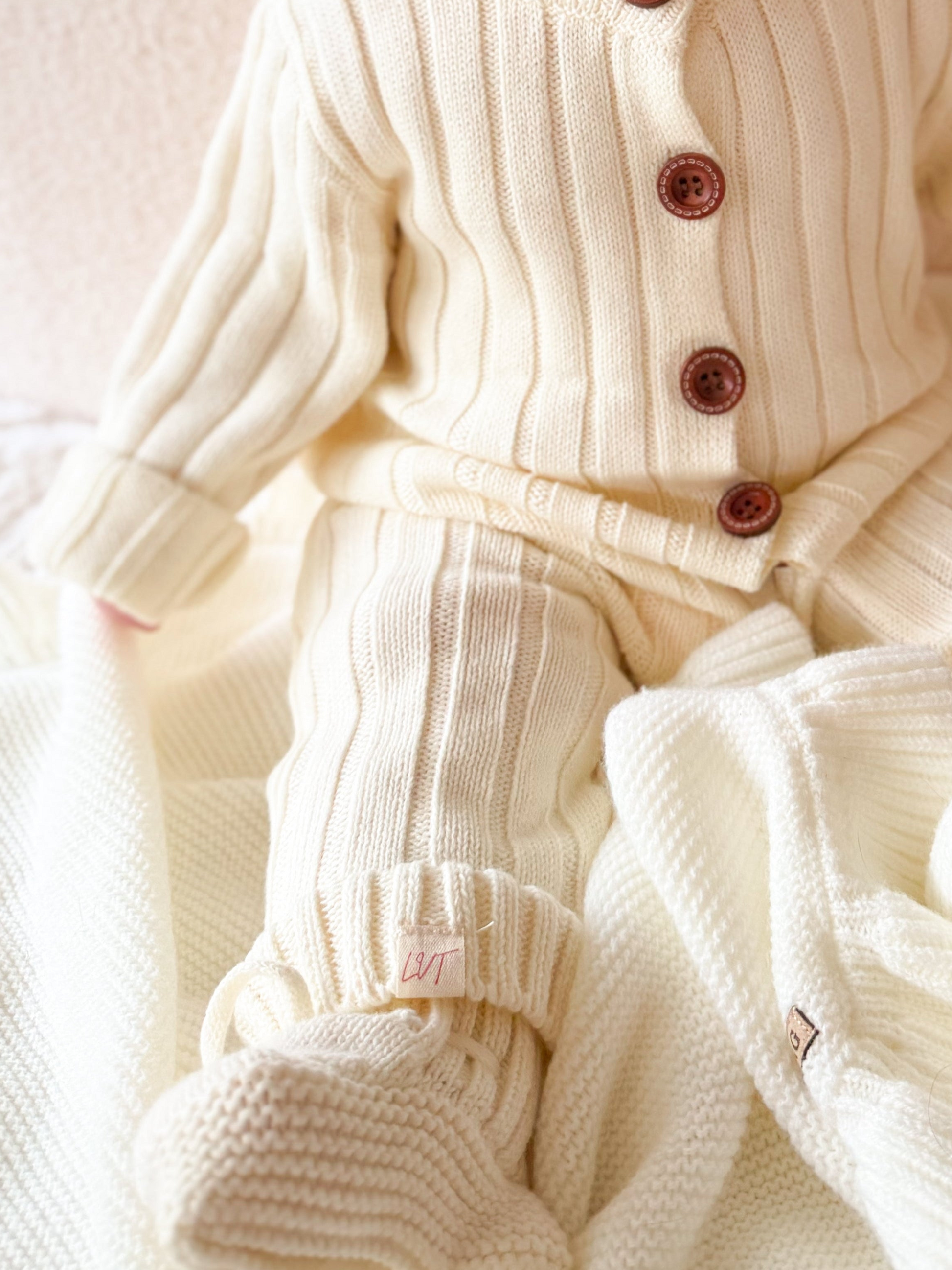 Close up of Vanilla Marshmallow baby knit booties in soft cream cotton knit with matching outfit and blanket