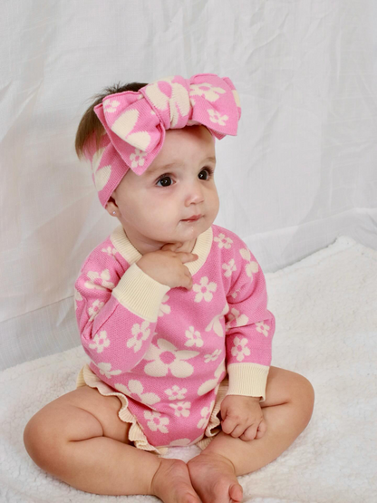 Baby wearing our Violet Knit Headband and matching pink floral knit romper sitting on a soft white backdrop