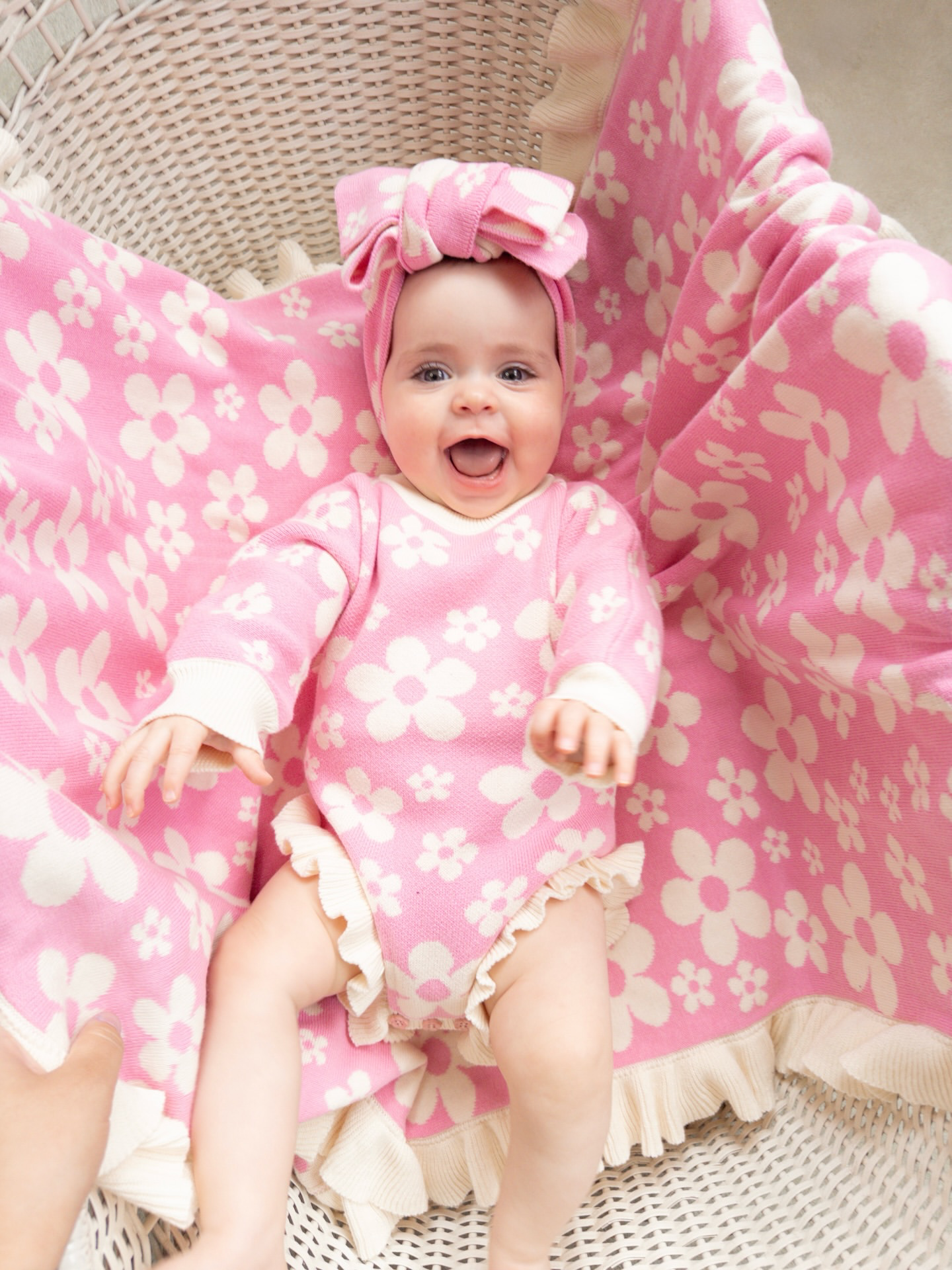 Happy baby sitting with our Violet Ruffle Baby Blanket and matching pink floral knit outfit in a cosy styled setting